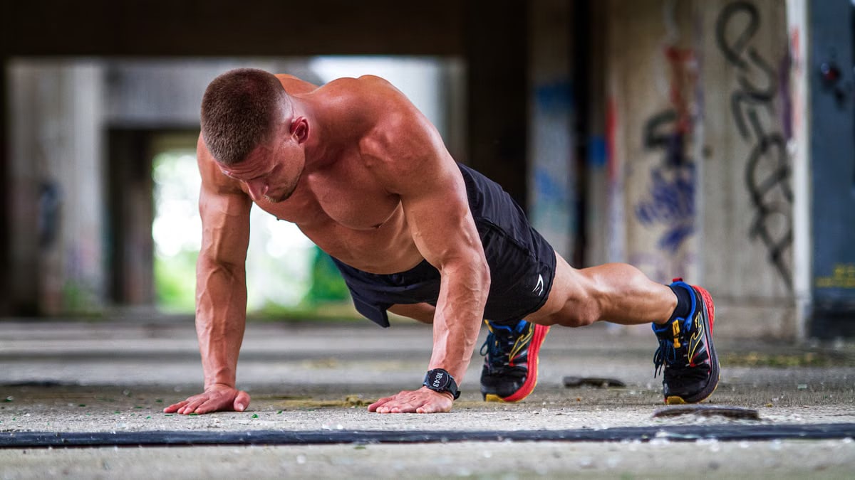 Shirtless caucasian man doing push-ups in an urban setting, showcasing strength and fitness.
